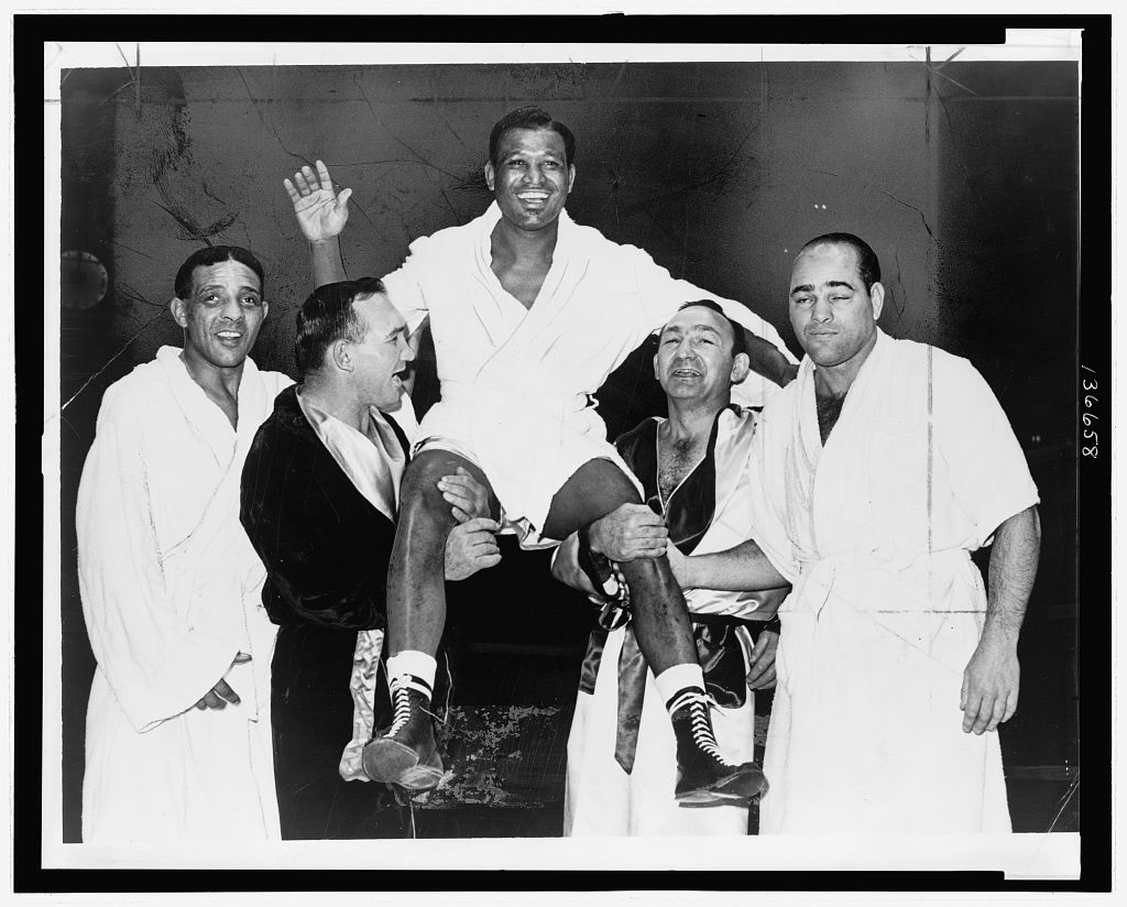 A black and white photograph of four men holding up boxer Sugar Ray Robison.