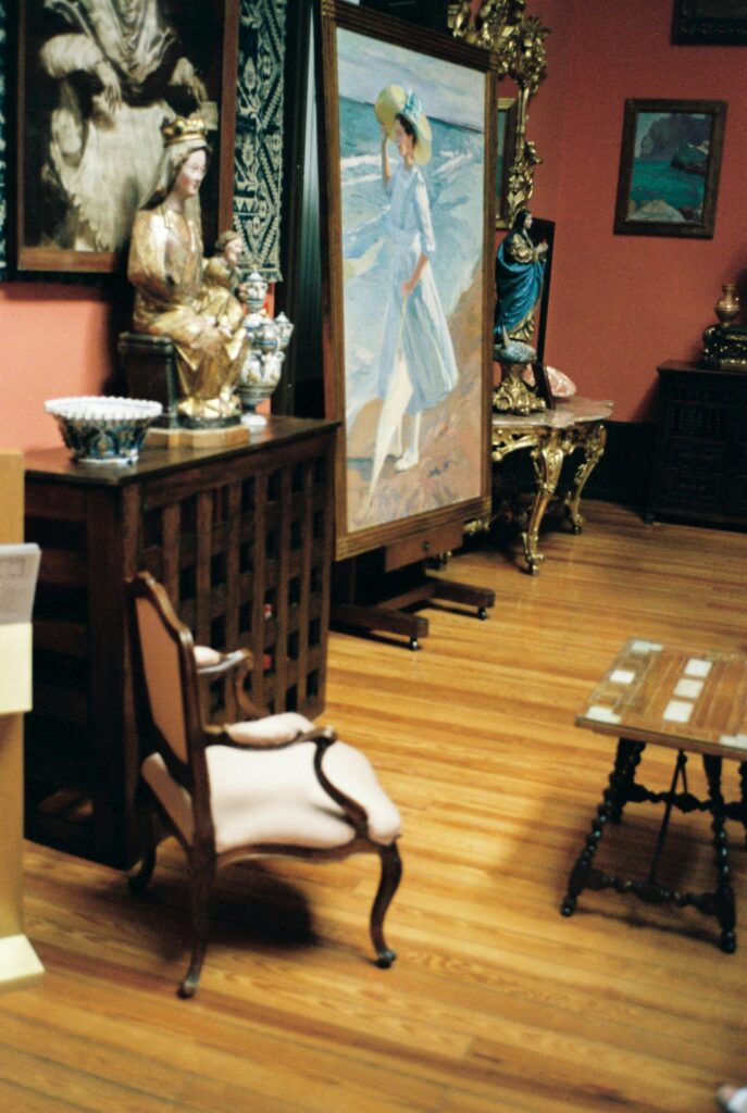 A photo inside a museum showing a chair, a painting and a decorated mantle.
