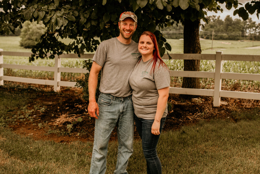 A man and a women standing next to each other in front of a white fence at Linden Hall Farm.